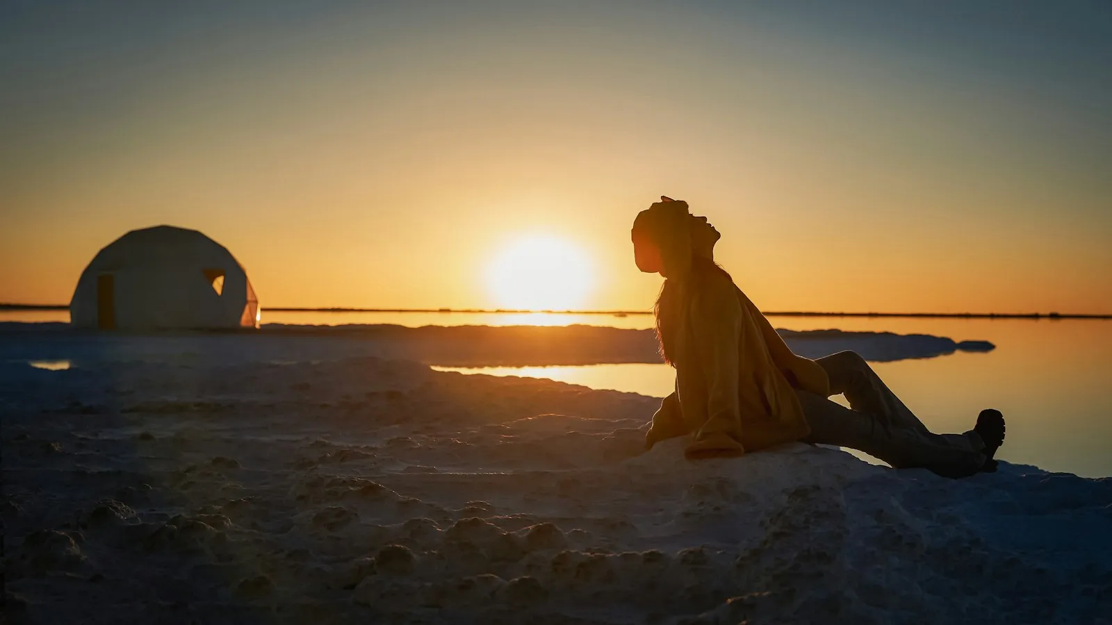 Silhouette d'une personne près d'une tente au bord de l'eau, à l'heure du coucher de soleil