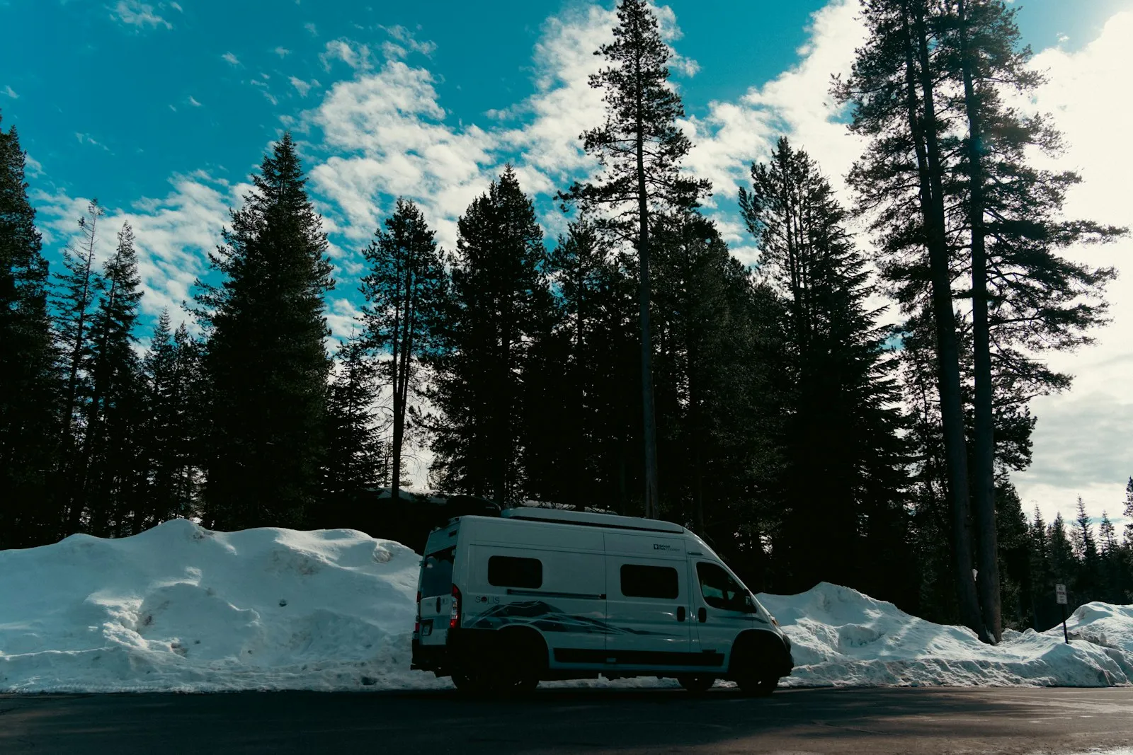 Van aménagé garé sur une route forestière enneigée, entouré de sapins en plein hiver