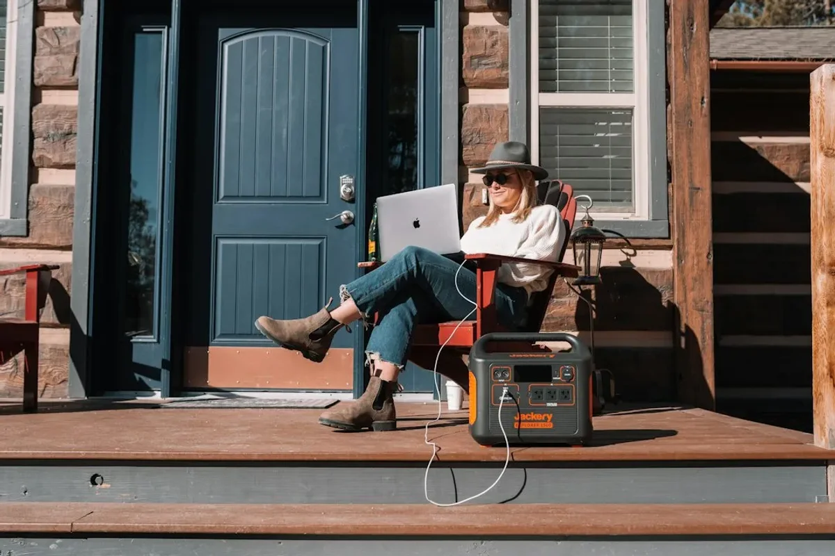 Personne assise en extérieur avec une station électrique portable posée au sol pour recharger son matériel