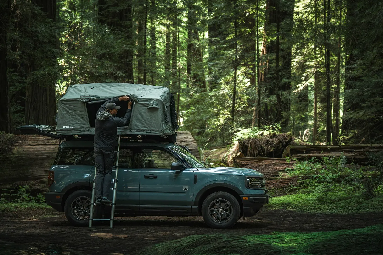 Une personne déplie une tente de toit installée sur un SUV garé dans une forêt