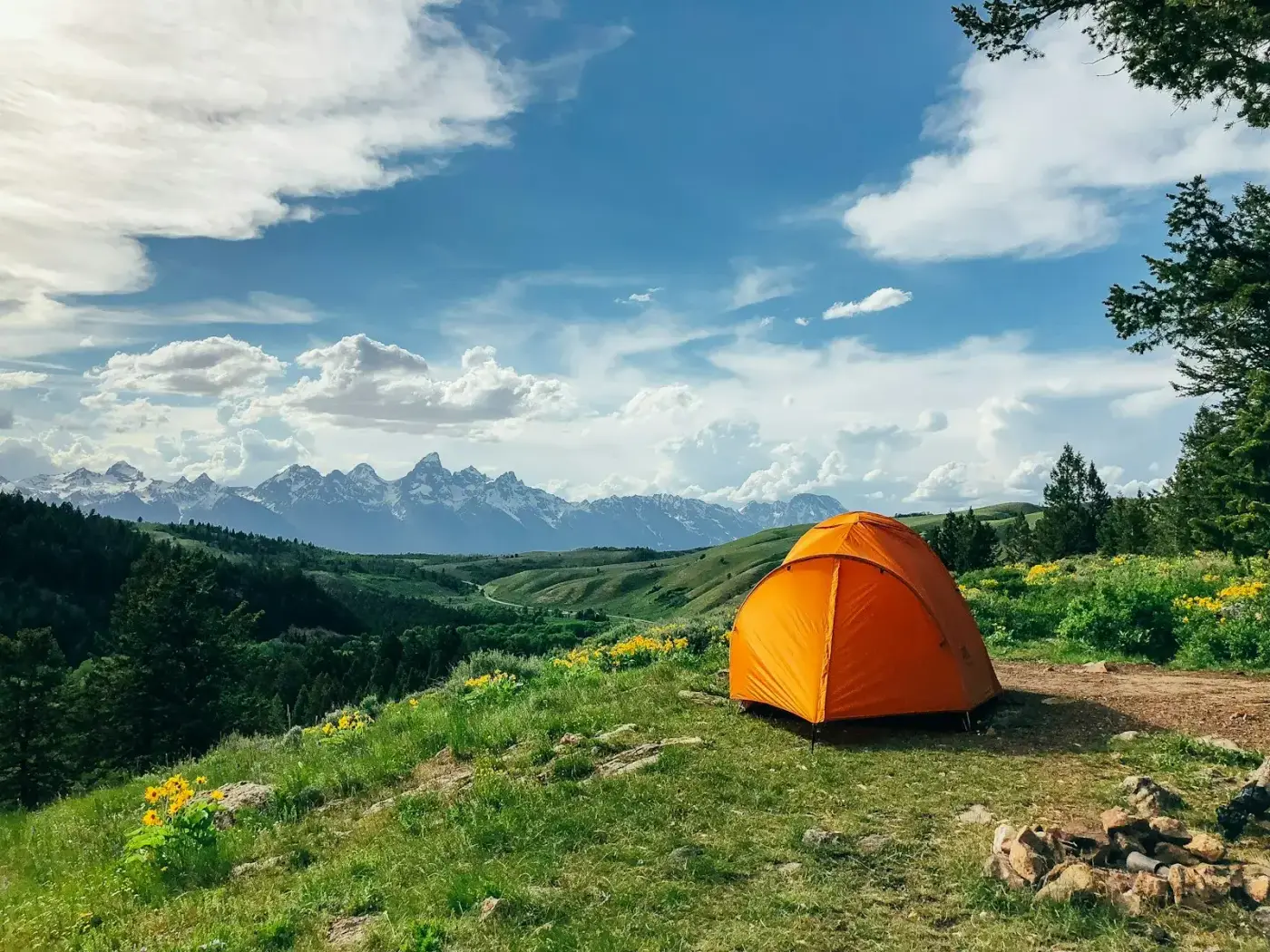 Tente orange plantée dans un pré, face aux montagnes