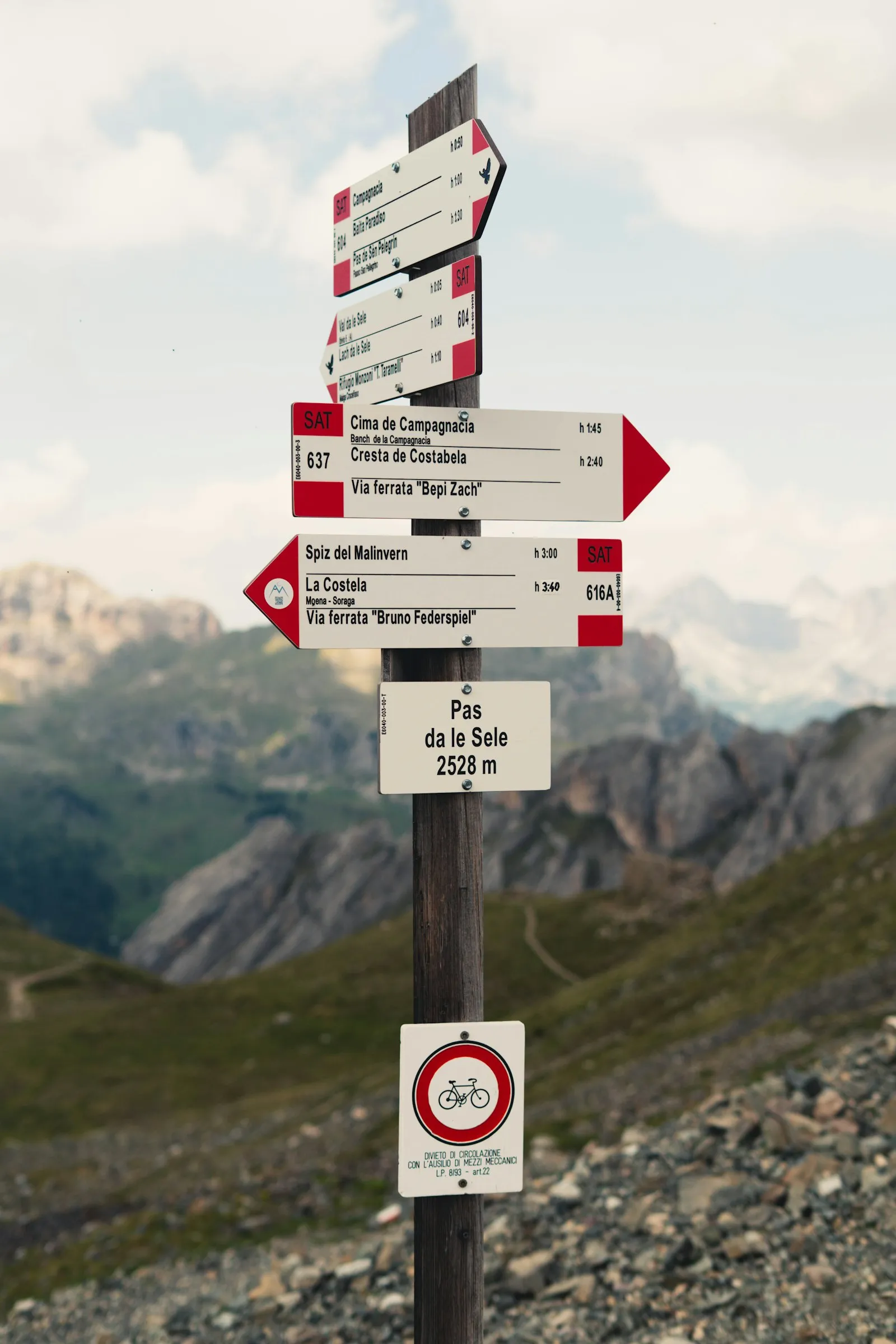 Panneau de randonnée avec plusieurs flèches directionnelles, planté dans un paysage de montagne rocailleux