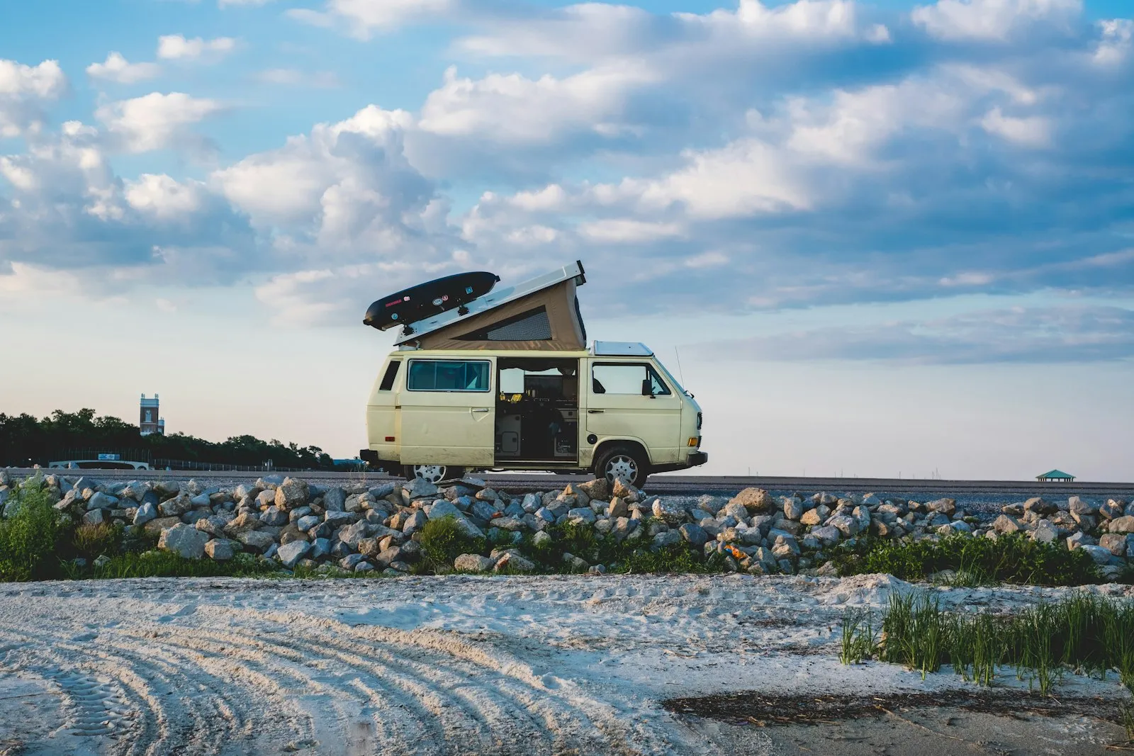 Combi crème au toit relevable déplié et coffre de toit, porte latérale ouverte, garé au-dessus d'une plage